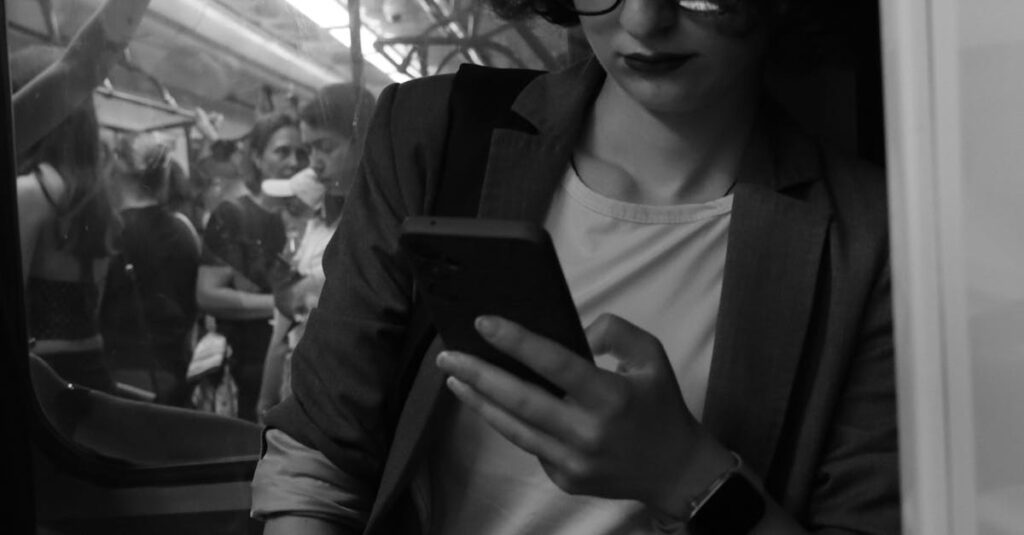 A woman in a suit reads her smartphone on a busy subway train in black and white.