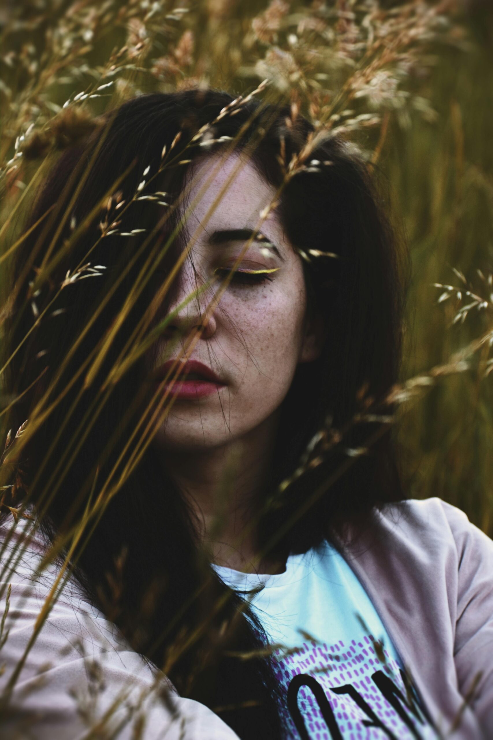 A contemplative woman partially obscured by grasses in a sunlit wheat field.