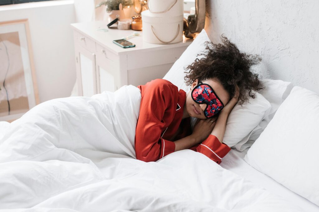 A woman in red pajamas sleeping with an eye mask in a bright, stylish bedroom.