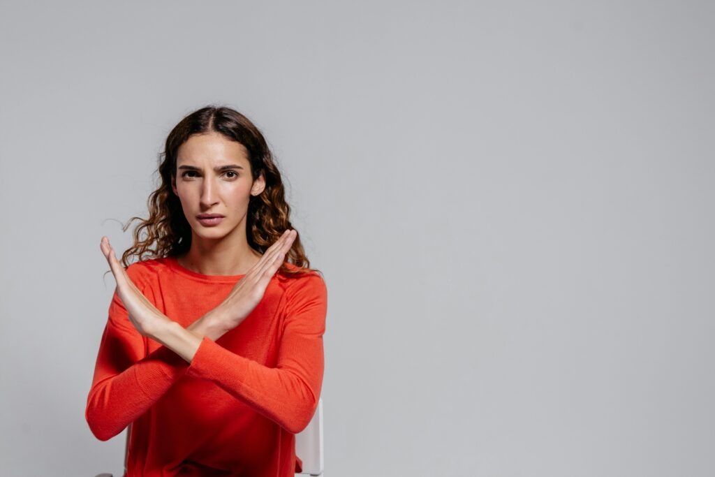 Woman with crossed arms making an X gesture against a gray background, indoor portrait.