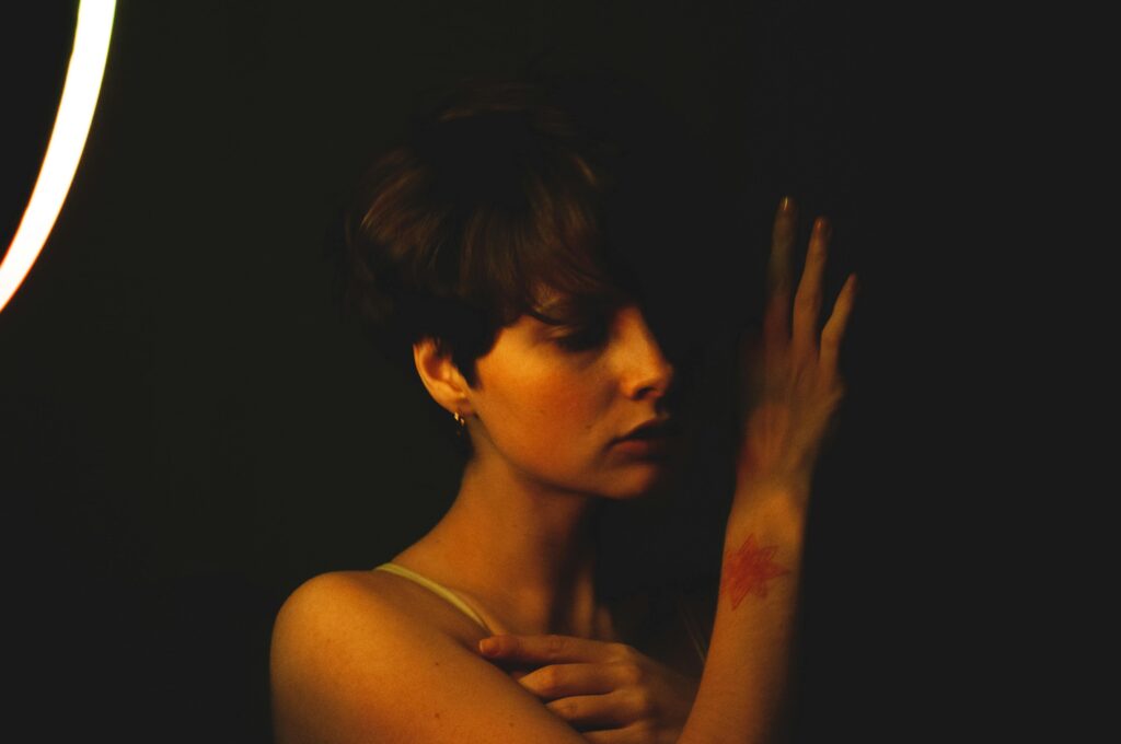 Artistic portrait of woman with short hair and tattoo, moody lighting, side view.
