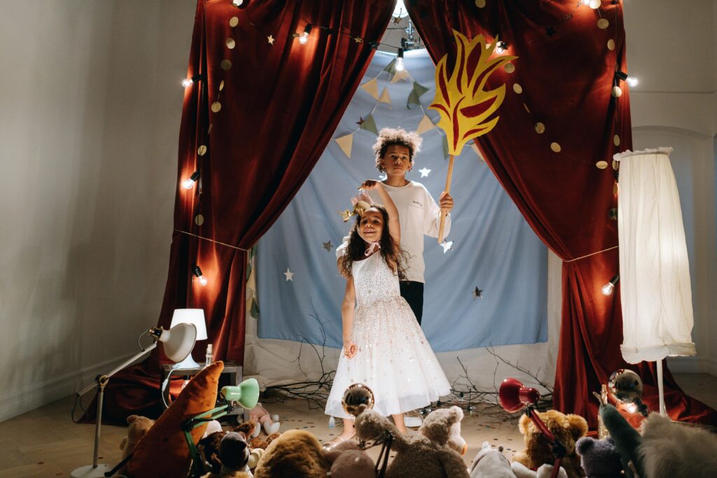Two children in a fantasy-themed play with costumes and props on a decorated stage.